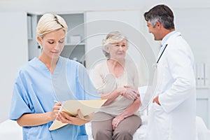 Female nurse making reports while doctor and patient shaking hands