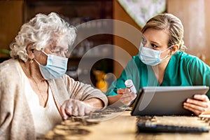 Female nurse reviewing prescription bottle with senior patient during home visit