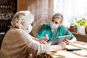 Female nurse reviewing prescription bottle with senior patient during home visit