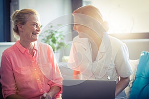 Female nurse and senior woman smiling while using laptop