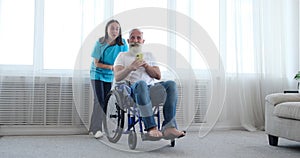 Female nurse taking care of disabled elderly man using mobile phone on wheelchair