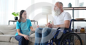 Female nurse talking to senior patient on wheelchair at home