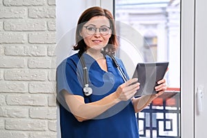 Female nurse using digital tablet computer, doctor near window in clinic office