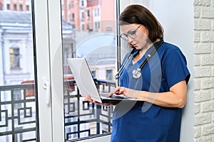Female nurse using laptop computer, doctor near window in clinic office