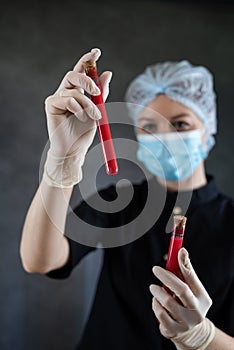 Female Nurse wearing black uniform mask and gloves holding blood in test tube