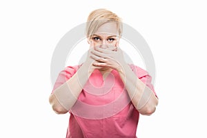 Female nurse wearing pink scrubs covering mouth like mute concept