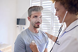 Female Nurse Wearing Uniform Listening To Male Patient\'s Chest In Private Hospital Room