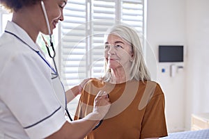 Female Nurse Wearing Uniform Listening To Senior Woman Patient's Chest In Private Hospital Room