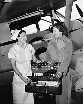 Female nurse with a young woman standing in front of an airplane and opening a medicine box