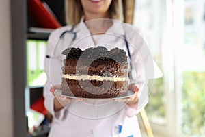 Female nutritionist holding large chocolate cake in hands