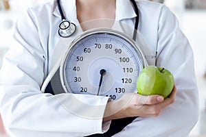 Female nutritionist holding weight scale and apple in the consultation.