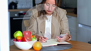 A female nutritionist sits at her desk and consults a patient over the phone and draws up a nutrition plan