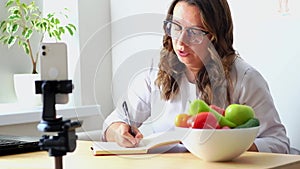 A female nutritionist sits at her desk and consults a patient over the phone and draws up a nutrition plan