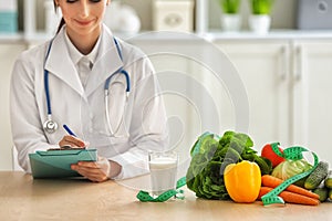 Female nutritionist sitting at table with vegetables and glass of milk in her office photo