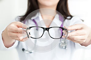 Female oculist doctor's hands giving a pair of black glasses