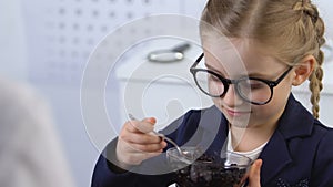 Female oculist giving blueberry bowl to kid in eyeglasses, eye health, vitamins