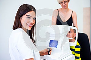 Female oculist using machine for checking eye sight in clinic. Little boy looking at equipment and doctor testing eye pupil in