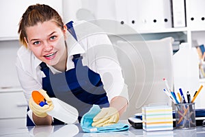 Female office cleaner is cleaning dust from the desk