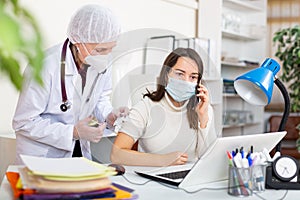 Female office employee in protective mask talking on phone during vaccination