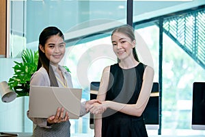 Female office person shaking hand working with laptop meeting in workplace. Two businesswomen happy success connection corporate.