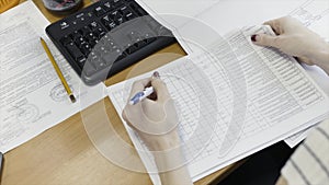 Female office worker doing paperwork at a desk with a computer, close up view. Action. Woman reading data report