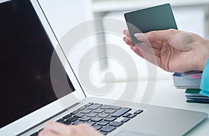 Female office worker hands holding credit card, typing on the keyboard of laptop, online shopping detail close up.