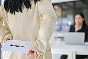 A female office worker hiding a resignation letter behind her back while talking with her boss