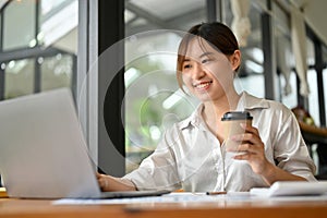 Female office worker or marketing staff using laptop computer and having a coffee