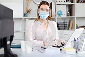 Female office worker in medical mask is having productive day at work in office