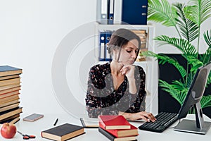 a female office worker in the office with a book at a desk in the office works at a laptop