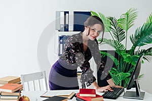 a female office worker in the office with a book at a desk in the office works at a laptop