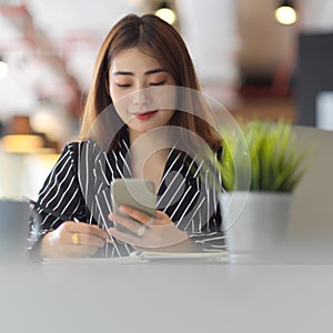 Female office worker using smartphone while sitting at worktable in office room