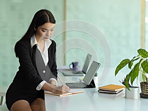 Female office worker working schedule book on desk with office supplies in co-working space