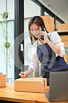 Female online shop owner preparing a customer`s package while talking on the phone