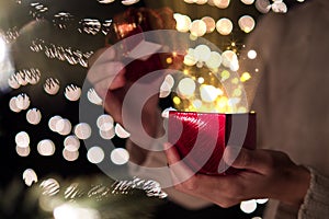 Female open red Christmas gift box with ray of magic light on bokeh lights background