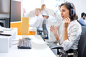 Female operator with headset talking to client with hands gesture and looking to computer at call center.