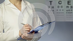 Female ophthalmologist writing down patient diagnosis and treatment, examination