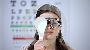 Female in optical trial frame closing eye and squeezing, poor vision problems