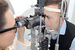 Female optician in surgery giving man eye test