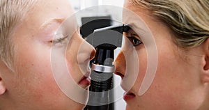 Female optometrist examining young patient with ophthalmoscope