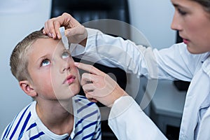 Female optometrist putting eye drop in young patient eyes