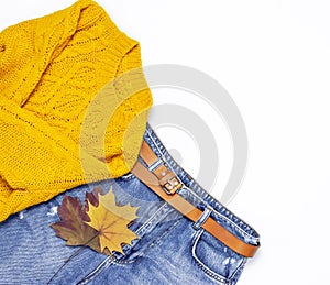 Female orange knitted sweater, blue jeans and autumn leaves on white background top view flat lay. Fashion Lady Clothes Set Trendy
