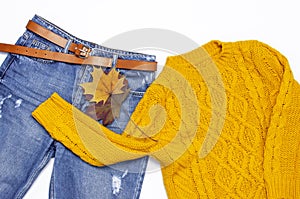 Female orange knitted sweater, blue jeans and autumn leaves on white background top view flat lay. Fashion Lady Clothes Set Trendy