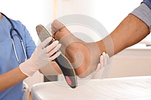 Female orthopedist fitting insole on foot in clinic, closeup