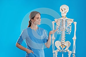 Female orthopedist with human skeleton model on background