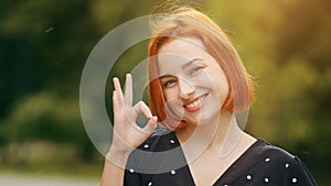 Female outdoors portrait happy caucasian woman model feminine lady shows okay hand gesture everything fine perfect sign