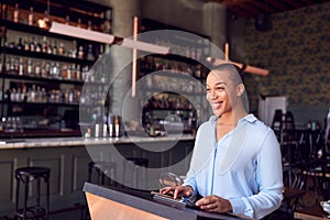 Female Owner Of Restaurant Bar Standing At Counter Using Digital Tablet