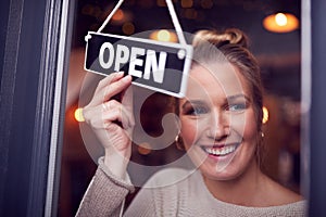 Female Owner Of Small Business Turning Round Open Sign On Shop Door