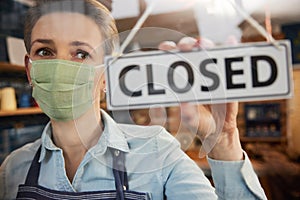 Female Owner Of Small Business Wearing Face Mask Turning Round Closed Sign During Health Pandemic
