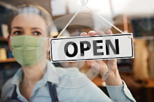 Female Owner Of Small Business Wearing Face Mask Turning Round Open Sign During Health Pandemic